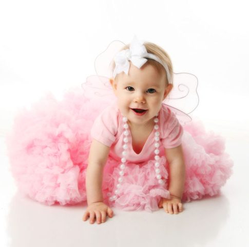 Portrait of a sweet infant wearing a pink tutu, necklace, and headband bow, isolated on white in studio